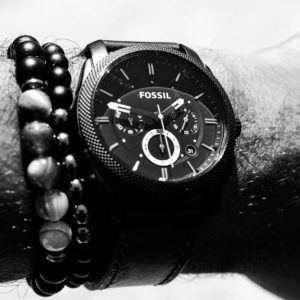 person wearing round Fossil chronograph watch with link band displaying 01:47 time